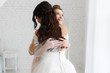 luxury bride hugging bridesmaid and smiling, joyful moment in minimalistic loft white brick background