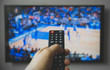 © M-Production - Male hand holding TV remote control. Basketball match.