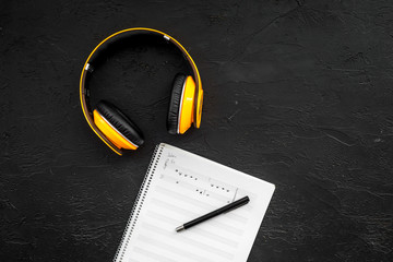 Work desk of modern composer. Music notes near headphones on black background top view copy space