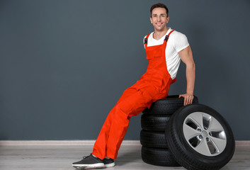 Wall Mural - Young mechanic sitting on stack of car tires near dark wall