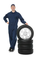 Poster - Young mechanic in uniform with car tires on white background