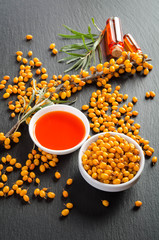 Wall Mural - Sea buckthorn with bottle and bowl with sea buckthorn oil isolated on black stone table. Top view.