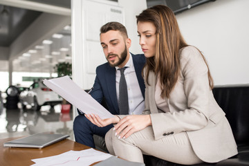 Portrait of two modern business people discussing documents in office  reading text