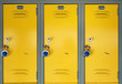Yellow school lockers with locks - Three locker doors of three yellow lockers in the hallway of a school, each with number plates, and a stainless steel combination lock with a blue knob on the face.