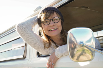 Mature trendy woman sitting in camper van by the beach