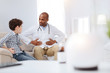 Pain area. Professional afro American male doctor and boy sitting on sofa while communicating and touching their bellies