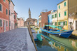 Typical canal with colorful facades with vibrant colors and Church of San Martino and its leaning campanile in famous fishermen village on the island of Burano, Venice, Italy