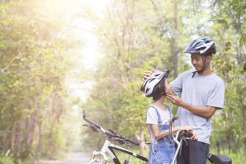 Wall Mural - Happy father and daughter cycling in the park wears a bicycle helmet to his daughter, togetherness relaxation concept