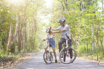 Wall Mural - Happy father and daughter cycling in the park wears a bicycle helmet to his daughter, togetherness relaxation concept