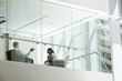 © Mint Images - Businessman and woman behind conference room window in large business center