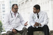 © Mint Images - Black and Hispanic male doctors discussing a case in a hospital hallway.