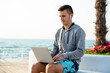 © Maksym Azovtsev - Sportive man using a laptop, sitting on bench, by the sea