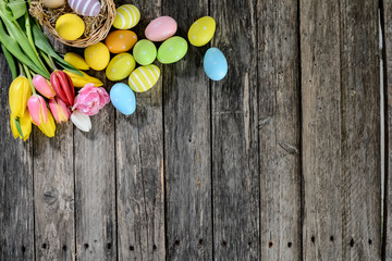 Wall Mural - above top view of multi colored painted easter eggs with springtime tulip bouquet flowers on a old wood plank