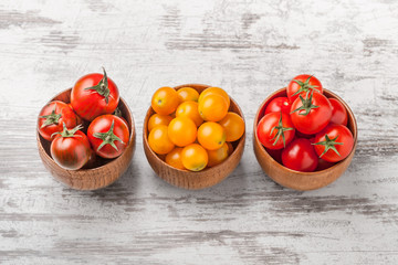 Wall Mural - Tomatoes in three wooden jars overhead arrangement on white rustic wooden background in studio