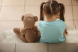Lonely little girl with teddy bear sitting on stairs. Autism concept