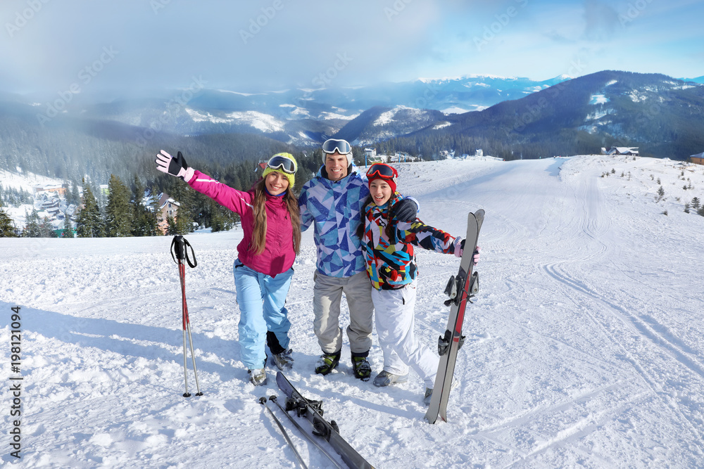 Happy friends on ski piste at snowy resort. Winter vacation