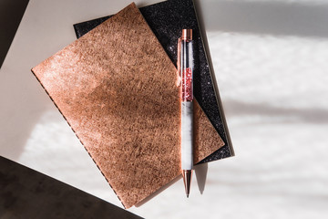 Glam rose golden and black glitter notepads with pen on white table. Morning sun lights. Minimalism fashion, beauty blogging, freelancing concept.