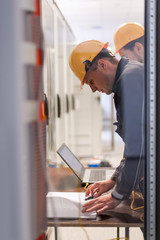 Wall Mural - two maintenance engineers inspect relay protection system with laptop comp