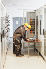 Wall Mural - two maintenance engineers inspect relay protection system with laptop comp