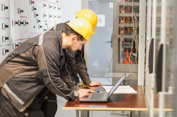 Wall Mural - two maintenance engineers inspect relay protection system with laptop comp