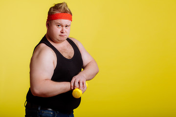 Fat man shows his muscle while holding dumbbell in hand