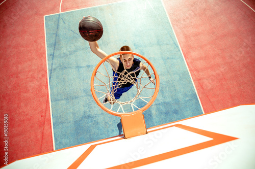 Fototapeta na drzwi i meble Młody człowiek skacze i robi fantastyczny wsad grając w streetball, koszykówkę. Miejskie autentyczne.