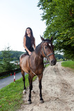 Fototapeta Konie - Pretty young woman riding a brown horse