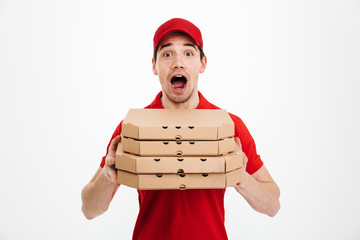 Wall Mural - Photo of emotional guy from delivery service in red t-shirt and cap holding stack of pizza boxes, isolated over white background