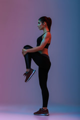 Wall Mural - Full length portrait in profile of caucasian woman with slim strong body doing workout and stretching her legs, isolated over colorful background