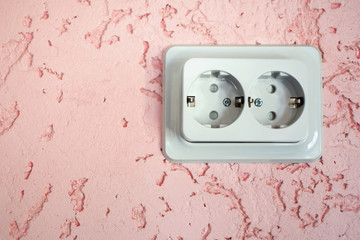  Light grey electrical socket on pink colored decorative plaster wall close up view with copy space for text.