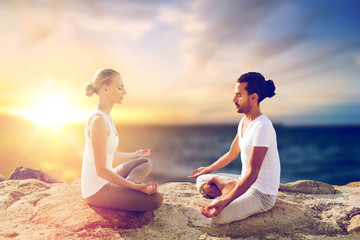 Canvas Print - yoga , mindfulness, harmony and people concept - happy couple meditating in lotus pose outdoors over sea background