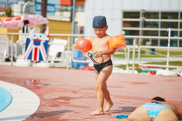 child in armlets for swimming in an outdoor pool with a water slide.