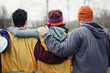 © Mint Images - View from behind of three friends with their arms around one another in sports kit and woolly hats.