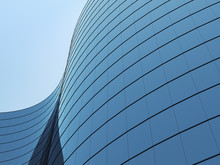 3D Stimulate Of High Rise Curve Glass Building And Dark Steel Window System On Blue Clear Sky Background,Business Concept Of Future Architecture,lookup To The Angle Of The Corner Building.