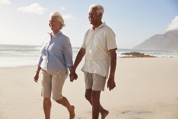 Senior Retired Couple Walking Along Beach Hand In Hand Together