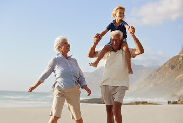 Wall Mural - Grandparents Carrying Grandson On Shoulders On Walk Along Beach