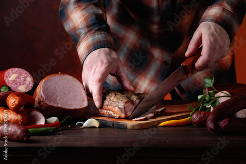 Zdjęcie XXL Mężczyzna kroi różne kiełbaski i wędzone mięso.