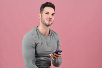 portrait of a young athletic man mysteriously smiling, looking up and holding a smartphone.