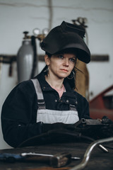 Wall Mural - Strong and worthy woman welder doing hard job in car and motorcycle repair shop. She using welding machine to fix some metal bike parts.