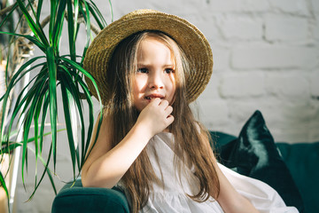 The cute little girl is lying on the green sofa\couch indoor plants around. Summer vacation begins.