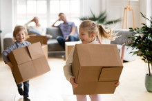 Active Children Enjoying Moving Day Running Carrying Boxes, Excited Kids Laughing Playing In New Home While Parents Take Break To Rest, Happy Girl And Boy Have Fun Together, Family Relocation Concept
