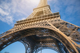 Fototapeta Paryż - The Eiffel Tower in Paris against the blue sky, the glare of the sun