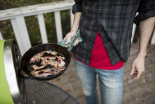 Midsection Of Man Holding Frying Pan With Bacon By Oven On Porch