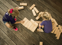High Angle View Of Sisters Playing With Wooden Toy Blocks While Crouching On Floor