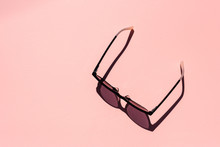 High Angle View Of Women's Tinted Glasses On Pink Background With Hard Shadows From Bright Sunlight (selective Focus)