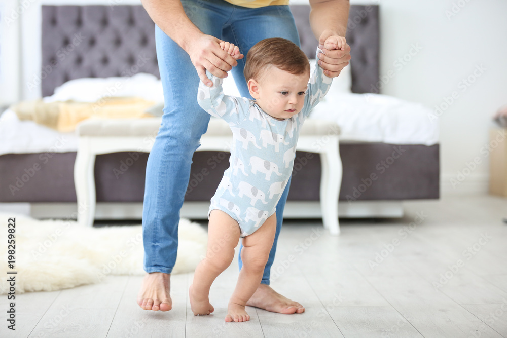Baby taking first steps with father's help at home - obrazy, fototapety, plakaty 