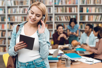 Wall Mural - Group of ethnic multicultural students in library. White girl using tablet listening to music.