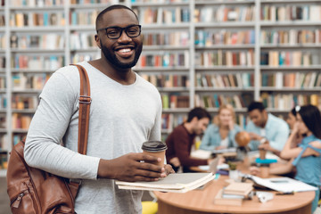 Wall Mural - Group of ethnic multicultural students in library. Black guy with notes and coffee.