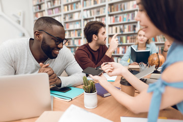 Wall Mural - Group of ethnic multicultural students in library. Asian girl showing phone to black guy.