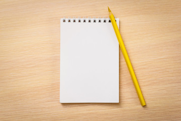 Yellow pencil with notebook on wooden table